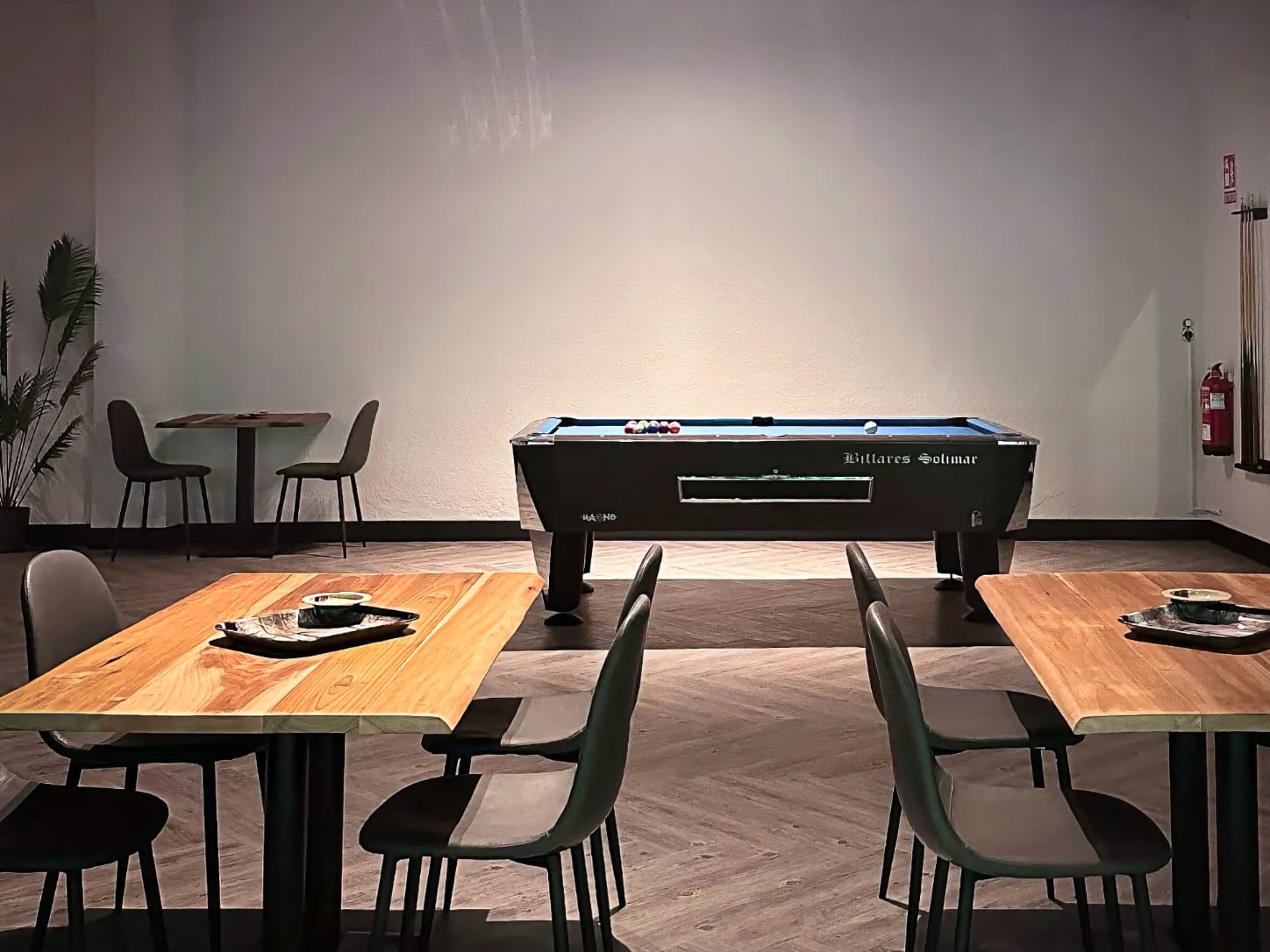 La zona de juegos del club de cannabis Four Twenty en Valencia, con una mesa de billar cl&aacute;sica Billares Solimar bajo una iluminaci&oacute;n ambiental, rodeada de mesas de madera y sillas.