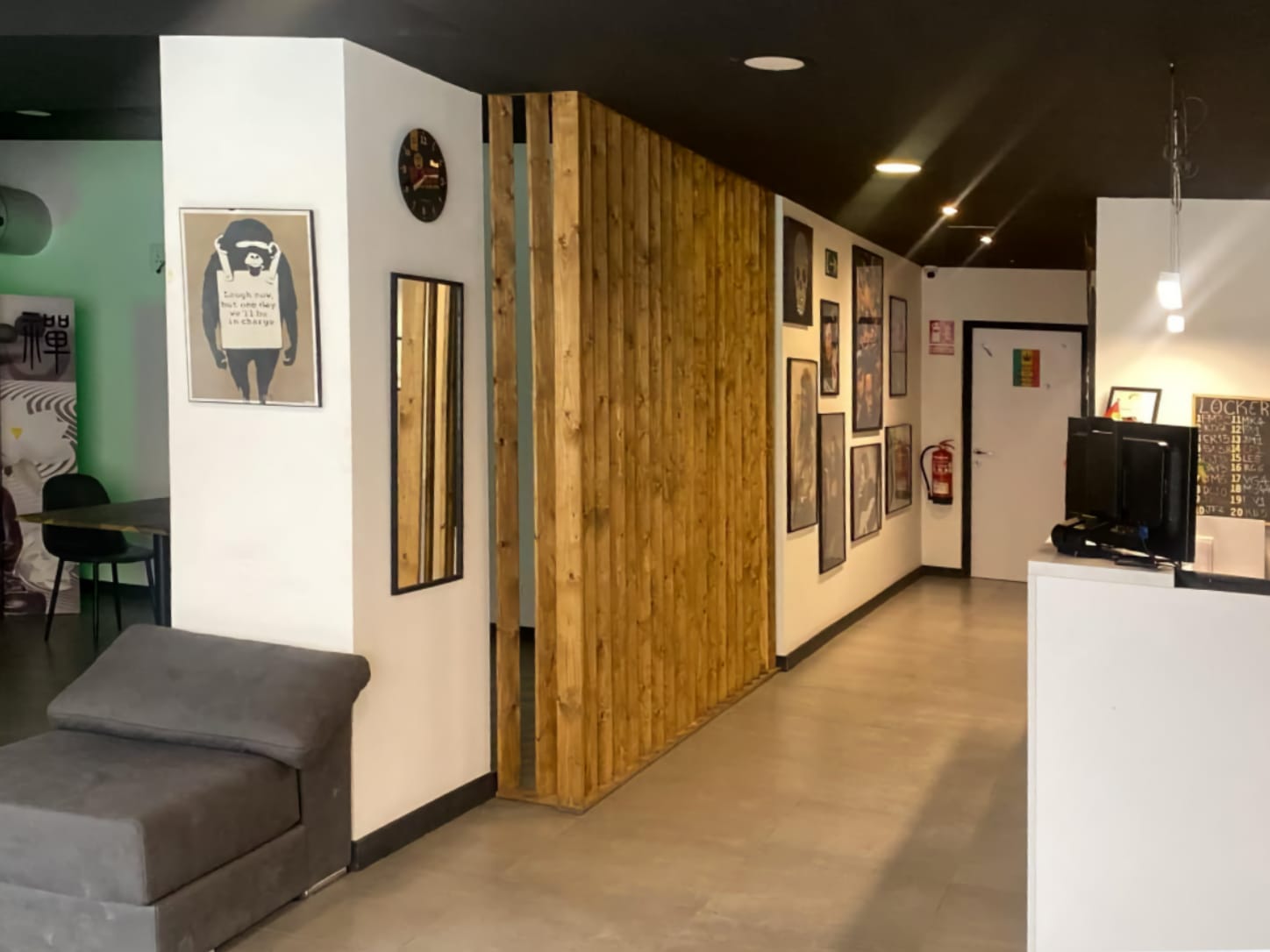 El mostrador de recepci&oacute;n y el moderno interior del club de cannabis Four Twenty en Valencia, con un tabique de lamas de madera, cuadros enmarcados y un sill&oacute;n gris.