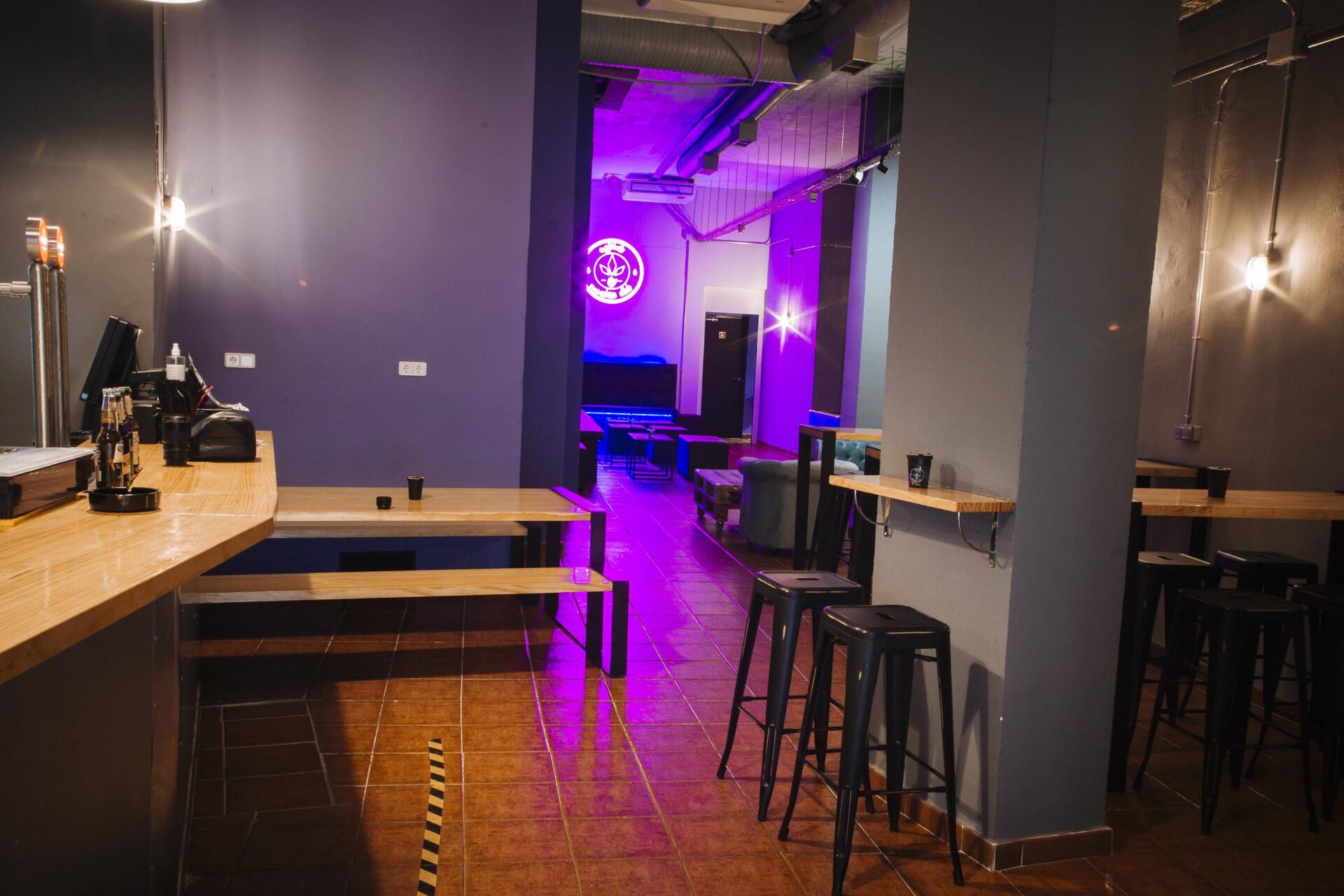 Zona de barra y mesas del club social cannábico Enjoint en Madrid con iluminación neón