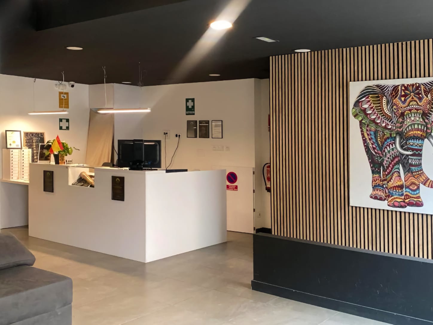 El mostrador de recepci&oacute;n blanco y minimalista del club de cannabis Four Twenty en Valencia, con iluminaci&oacute;n moderna y un colorido cuadro de un elefante en una pared de lamas de madera.