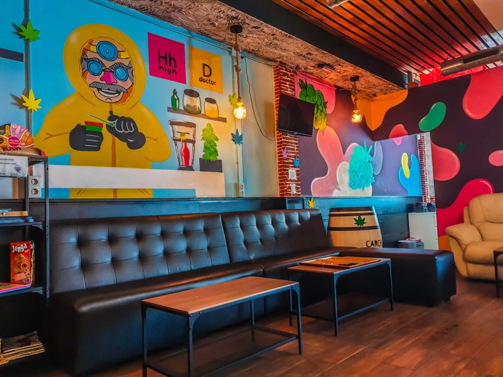 Interior del social club High Doctor en Alicante con paredes graffiti coloridas, sof&aacute;s cuero negro y suelo madera.