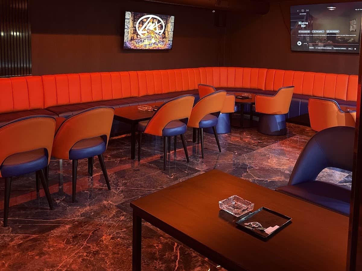 Interior del social club Lux Lounge en Marbella con sof&aacute;s de terciopelo naranja, pantalla TV y suelo de m&aacute;rmol.
