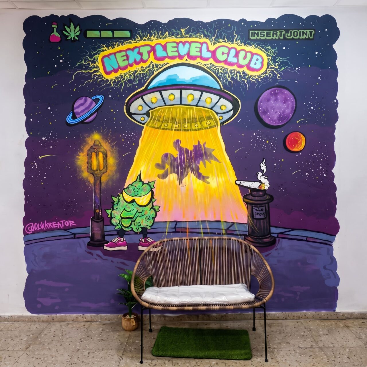 Interior del club de cannabis Next Level Club en Valencia: un banco trenzado frente a un graffiti de un OVNI.