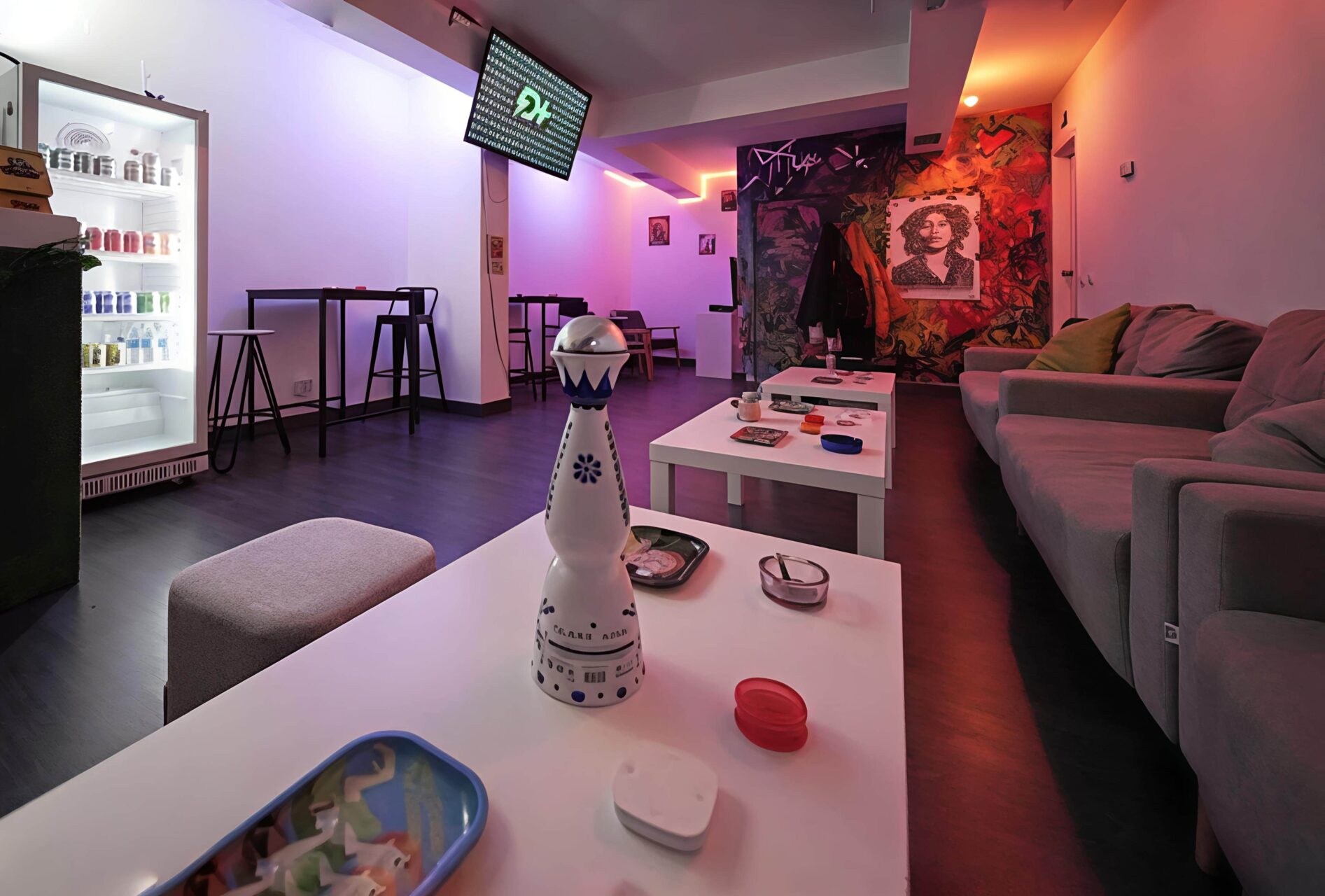 Zona de sal&oacute;n en el cannabis club Valhalla en Madrid con iluminaci&oacute;n de ne&oacute;n azul y naranja, mesas bajas y pared con graffiti.